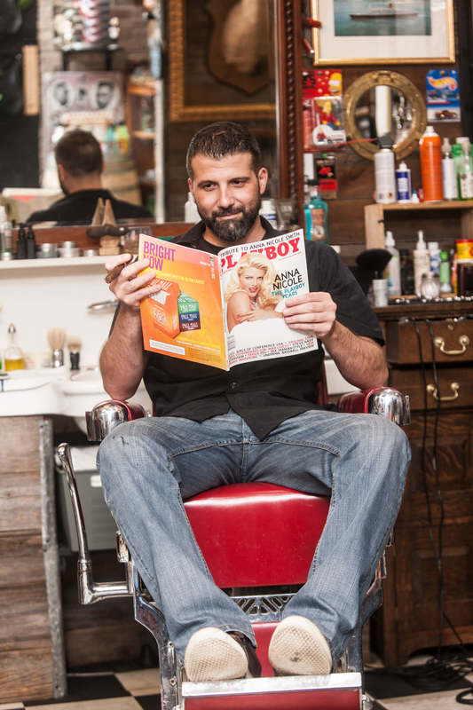 Rob from Back Alley Barber Shop on a barber chair reading a Playboy magazine